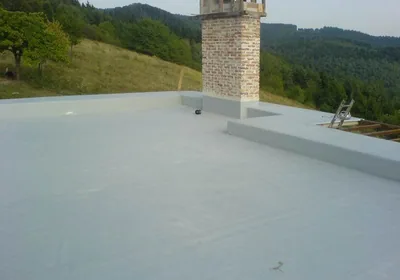 Plochá strecha s tehlovým komínom po položení fólie, v pozadí lesy