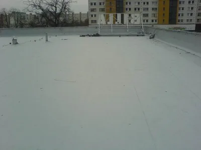 Sivá fólia na plochej streche, v pozadí paneláky